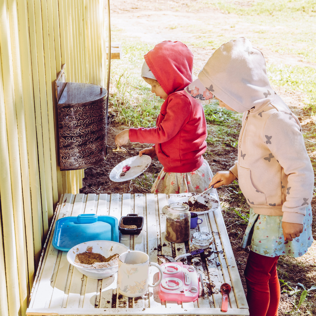 Two school age children playing in a "mud kitchen" outside