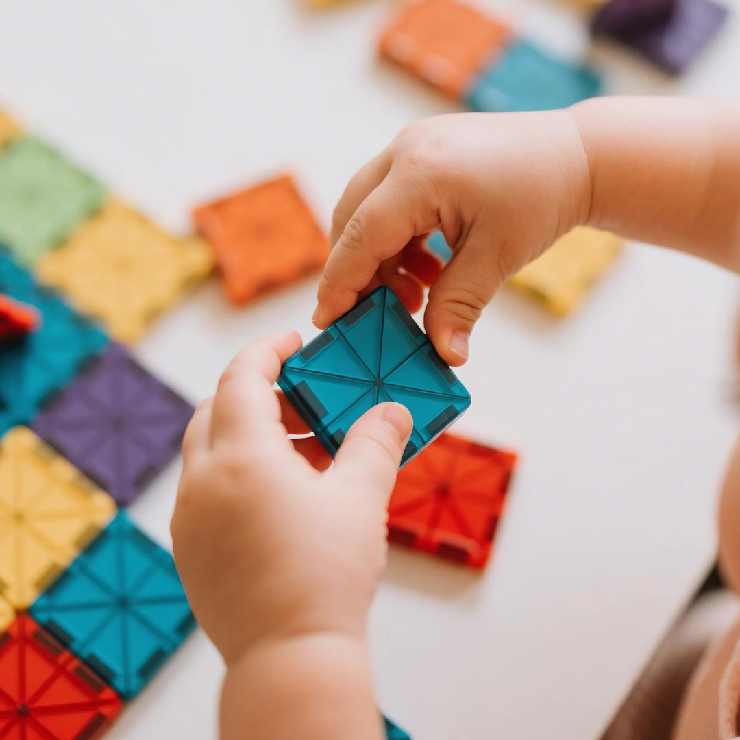 Young child's hands playing with colourful magnetic tiles