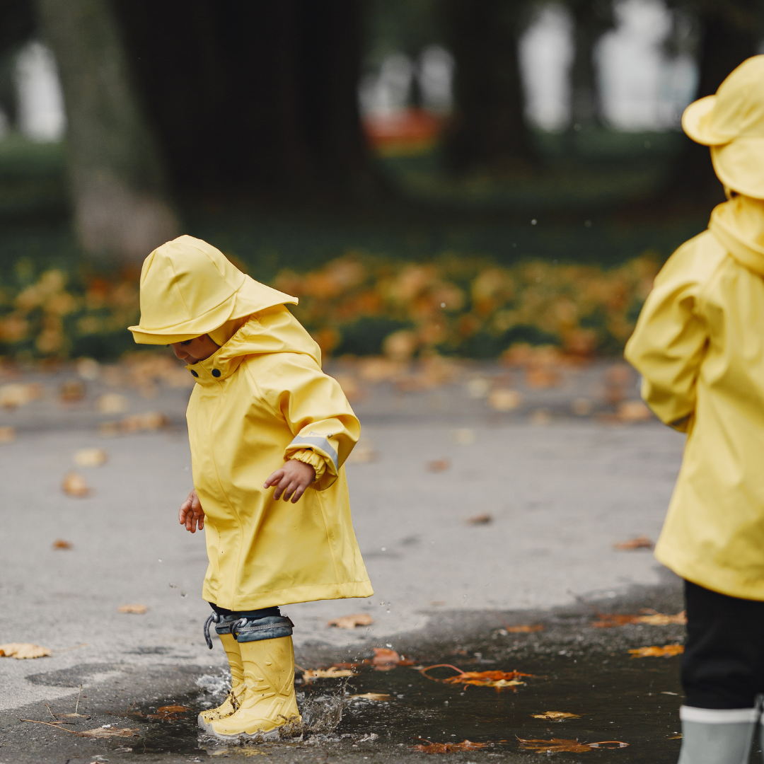Two kids in rainsuits and boots playing in puddles