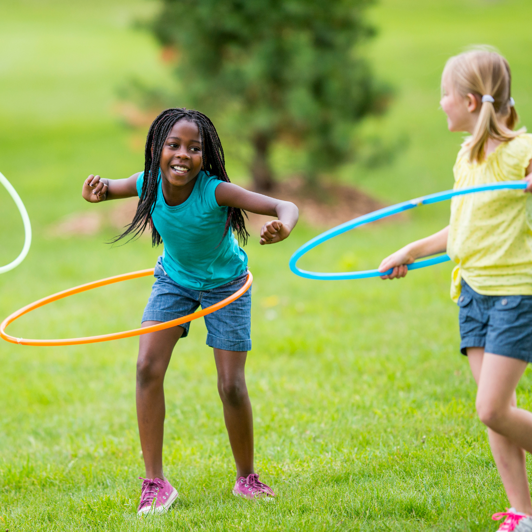 School age children hula hooping outside on the grass in a park