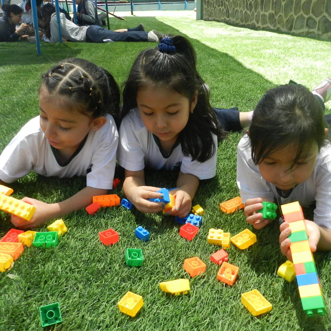 Three children outside lying on the grass, playing with blocks