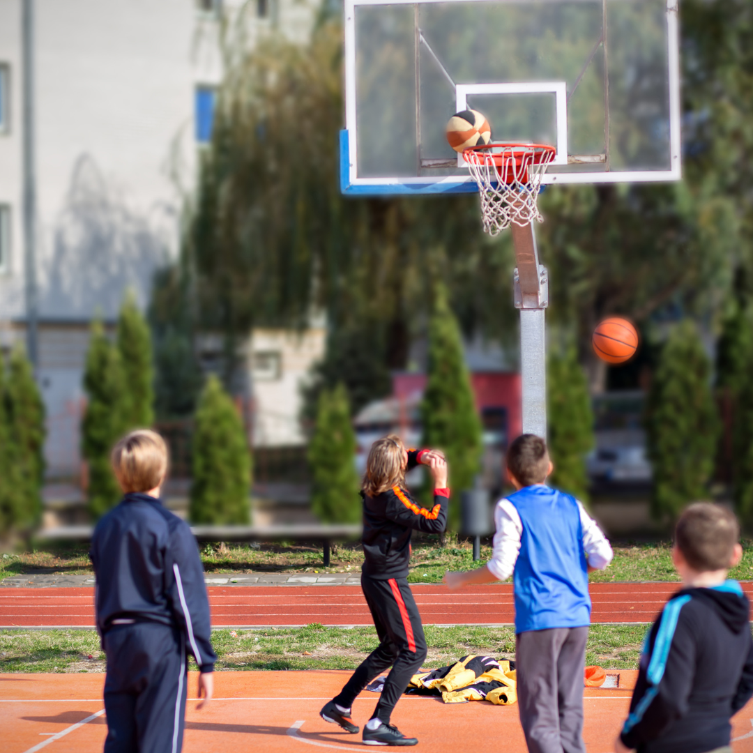 School age children playing basketball on a court outside