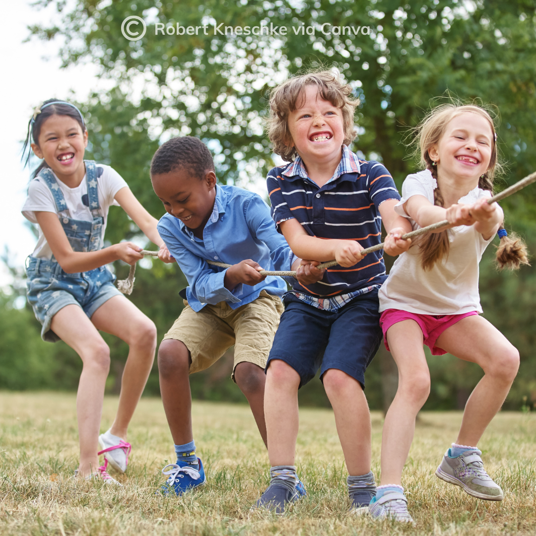 School age children working as a team, pulling a rope together outside on the grass