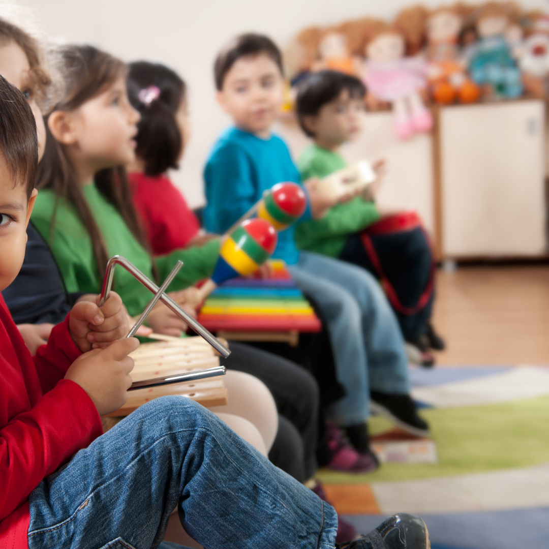 Children sitting on chairs, holding musical instruments like triangle, shakers, tambourine