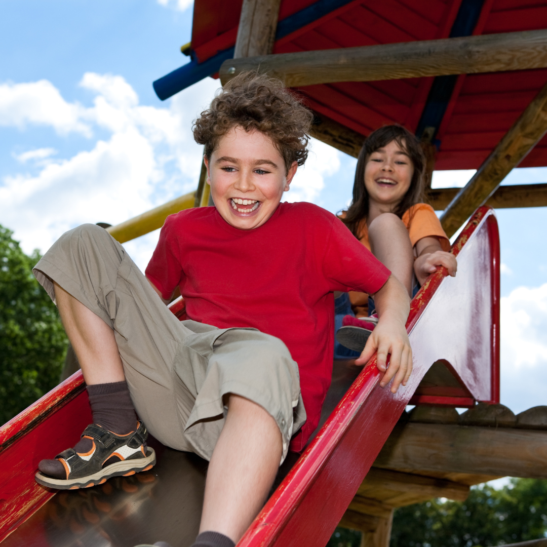 Two school age kids on slide in outdoor playground