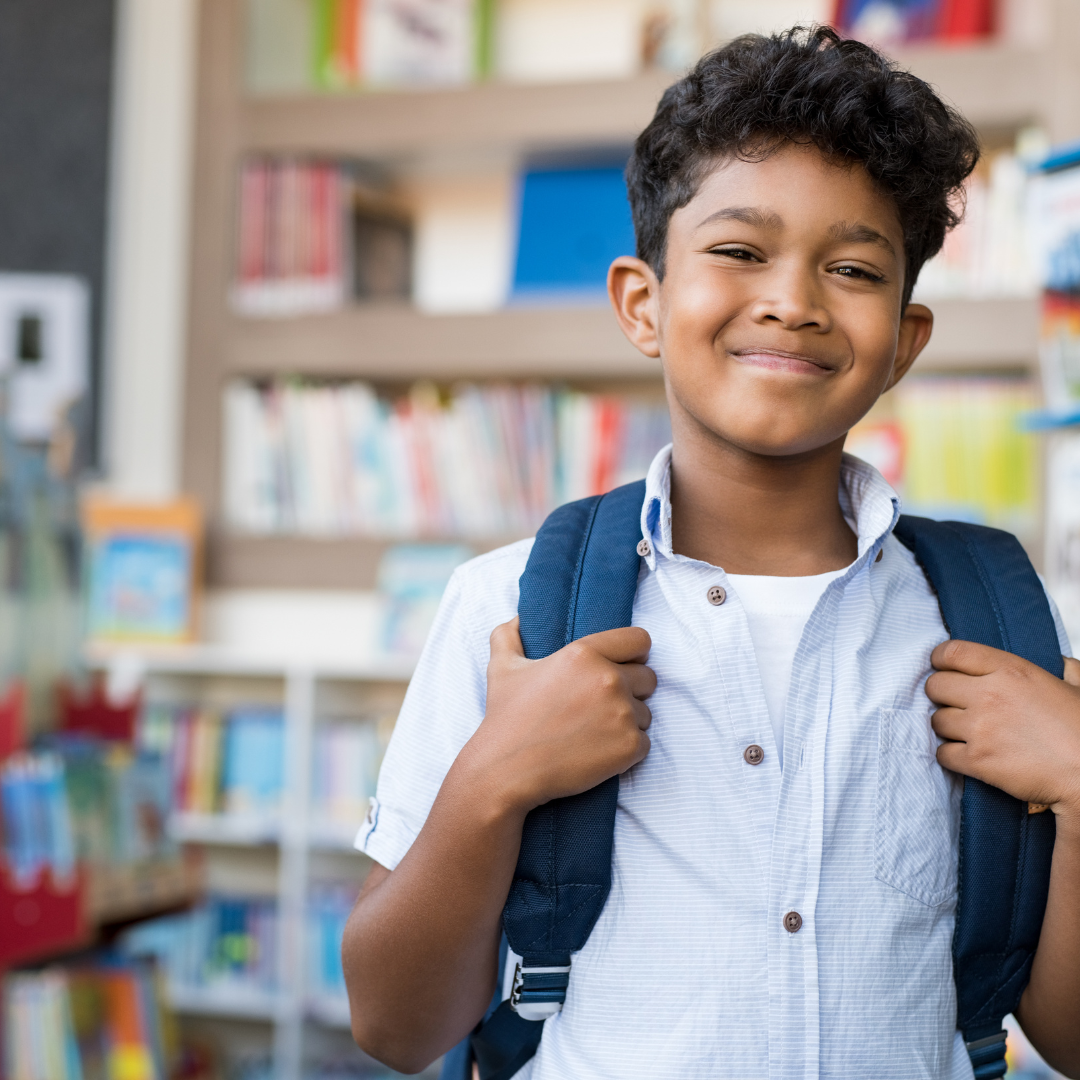 Smiling school age child wearing a backpack inside a classroom