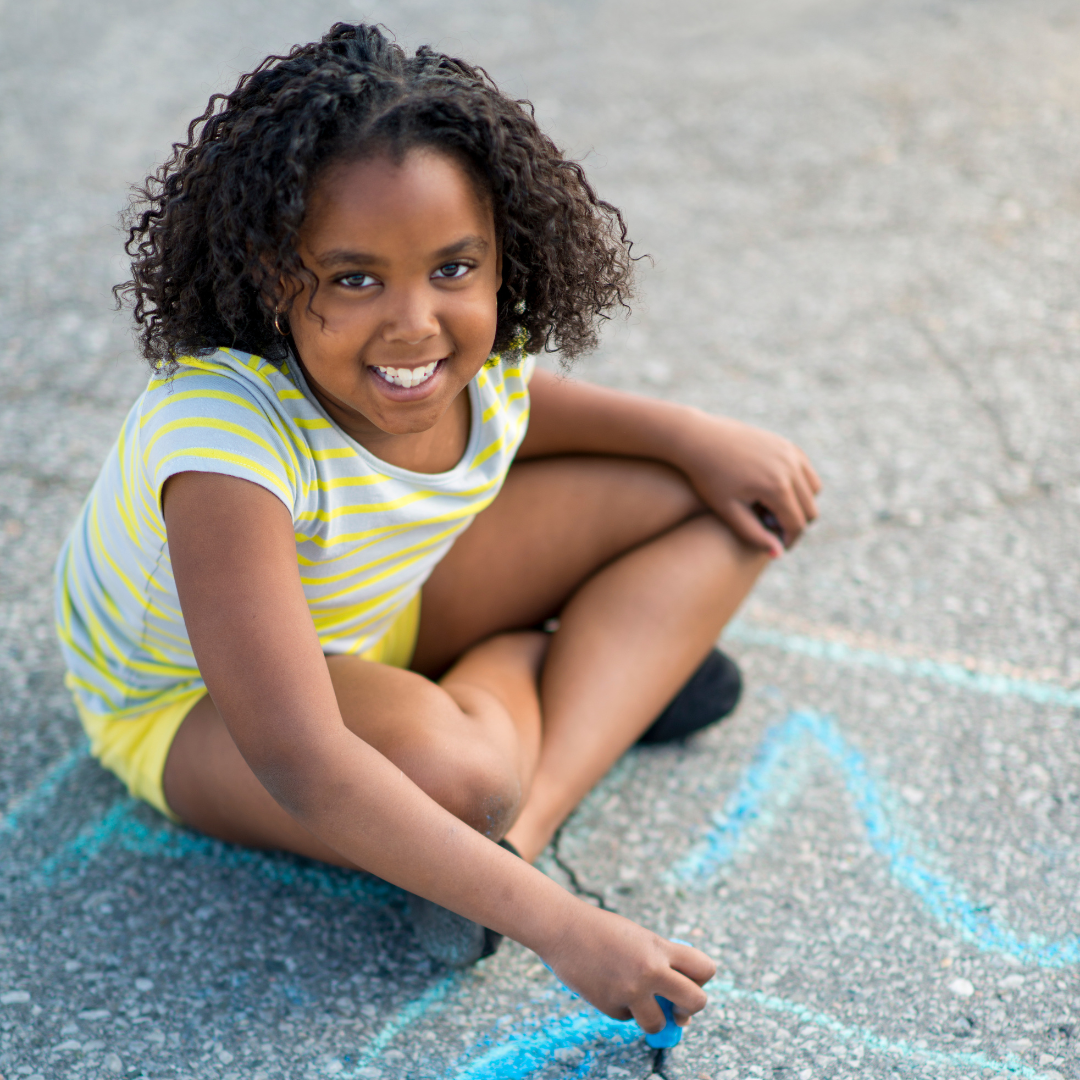 Child sitting on ground, playing with chalk