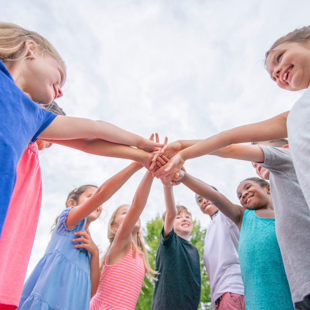 Kids standing a circle outside, putting their hands in together