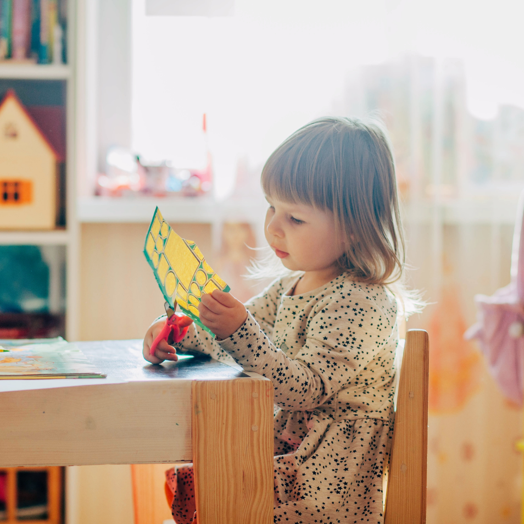 Preschooler sitting at a table and cutting with scissors