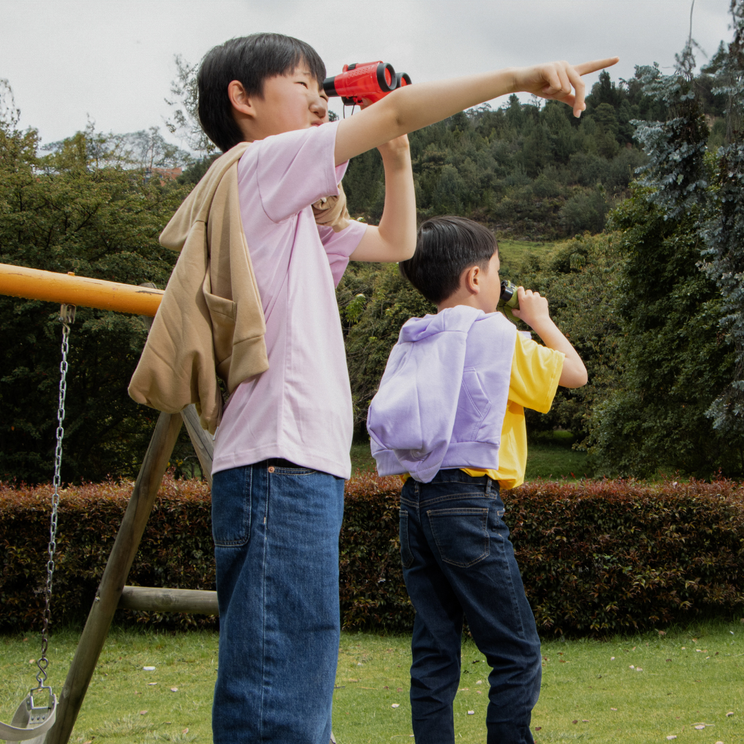 Two children outside in the daytime looking through binoculars