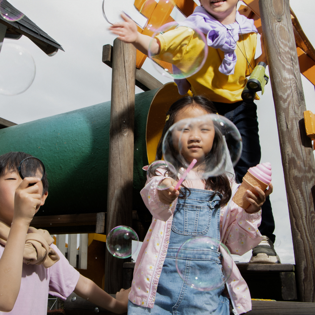 Children playing with bubbles, standing on outdoor playground structure