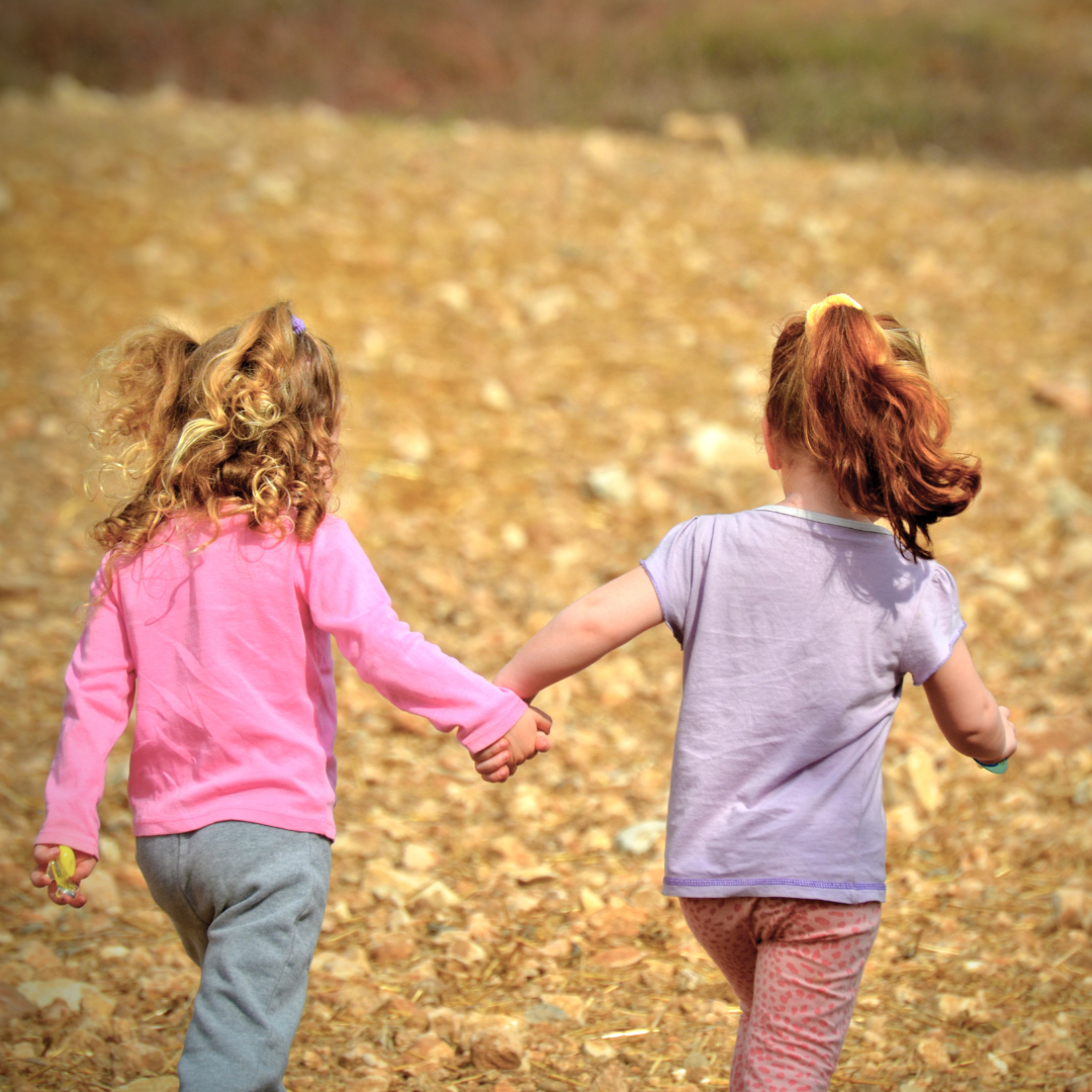 The backs of two kids who are holding hands and walking outside in Autumn