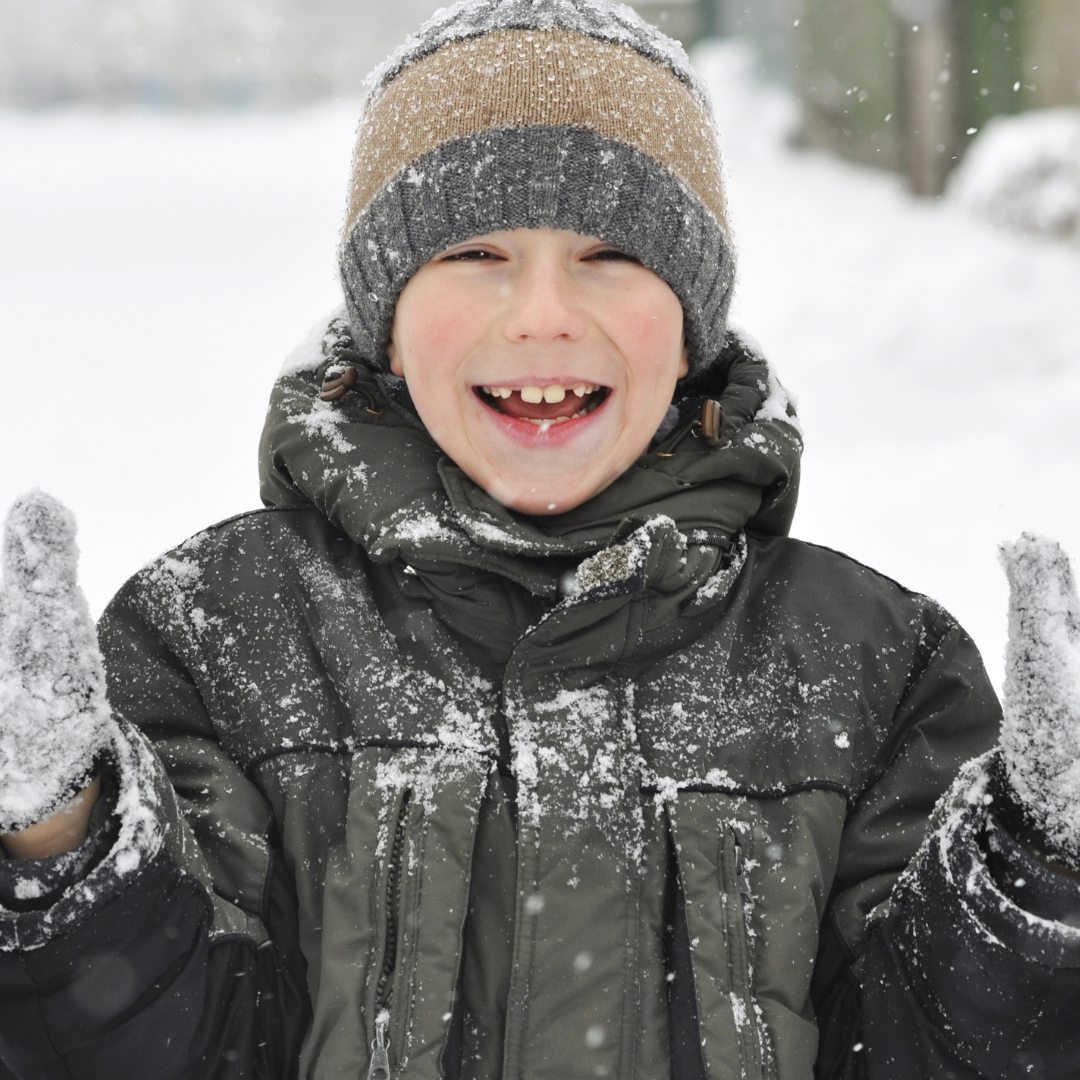 Smiling school age child standing in the snow with hands raised