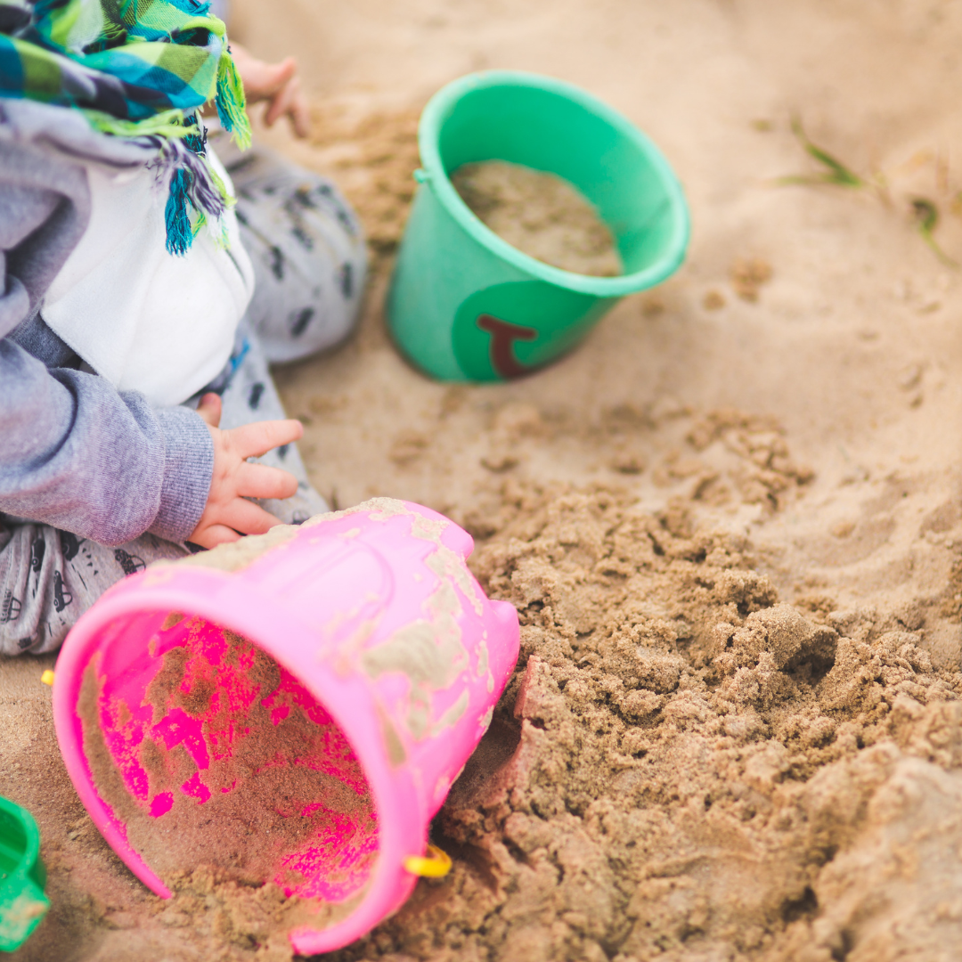 Child's hands playing in sand with buckets