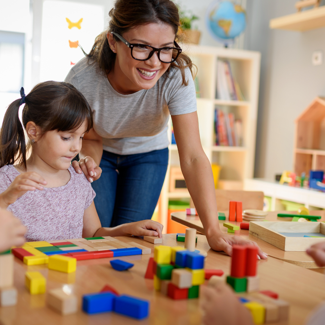 Preschool teacher beside child playing with blocks at table