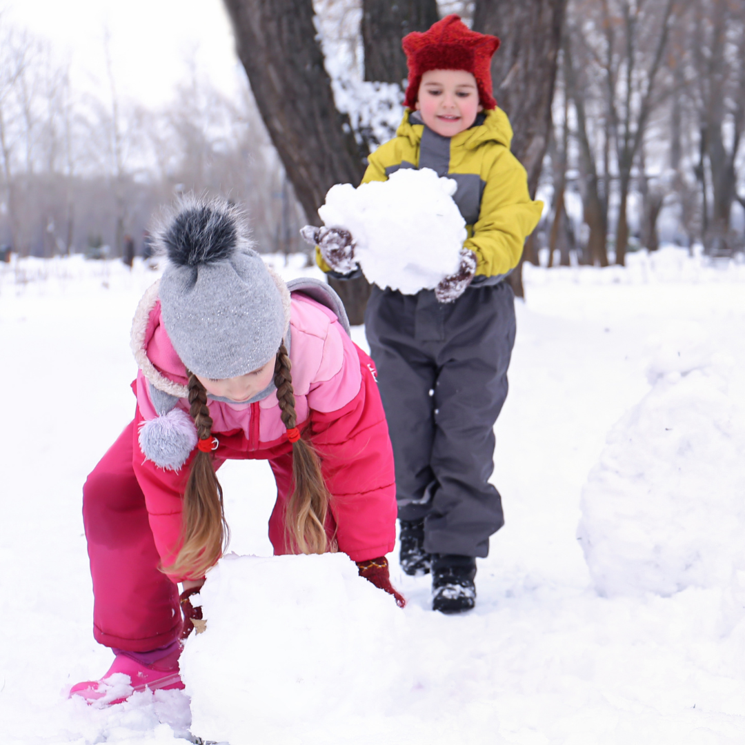 Two kids outside rolling snowballs