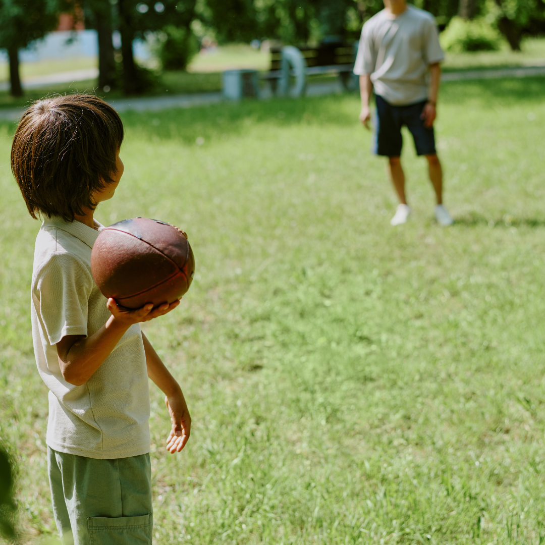 Child outside on grass, holding a football, about to throw to an adult