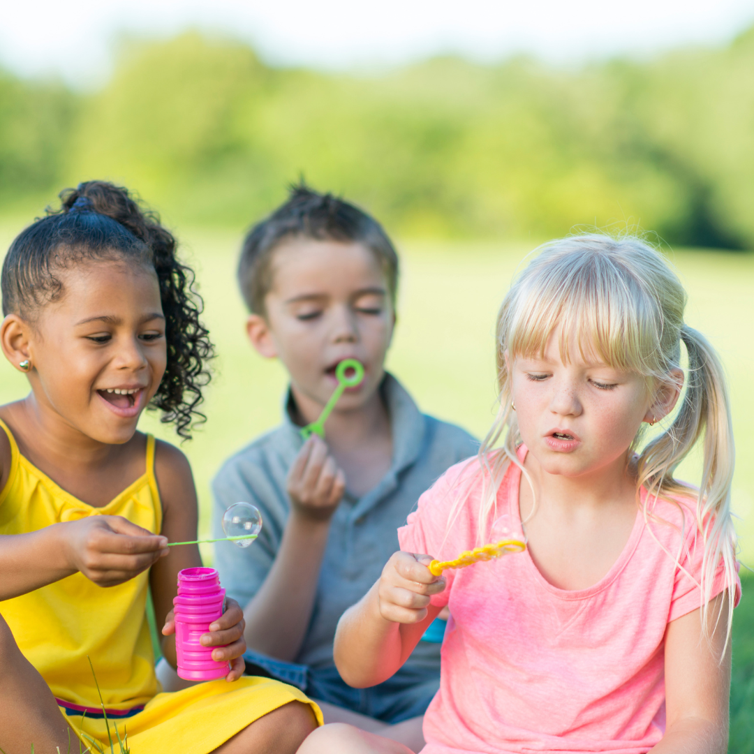 Children sitting on grass, blowing bubbles
