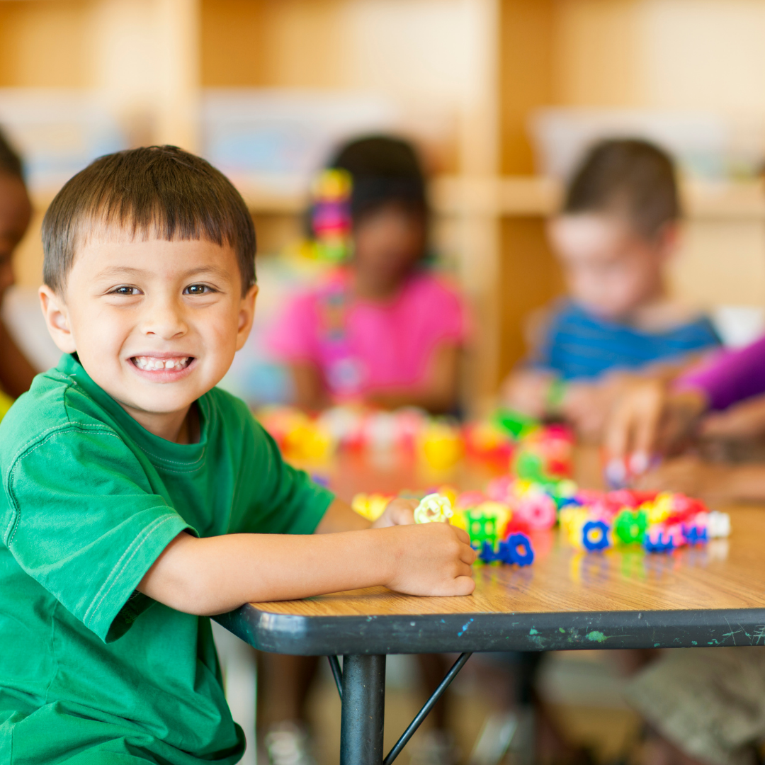 Smiling child doing table activities, other children in the background