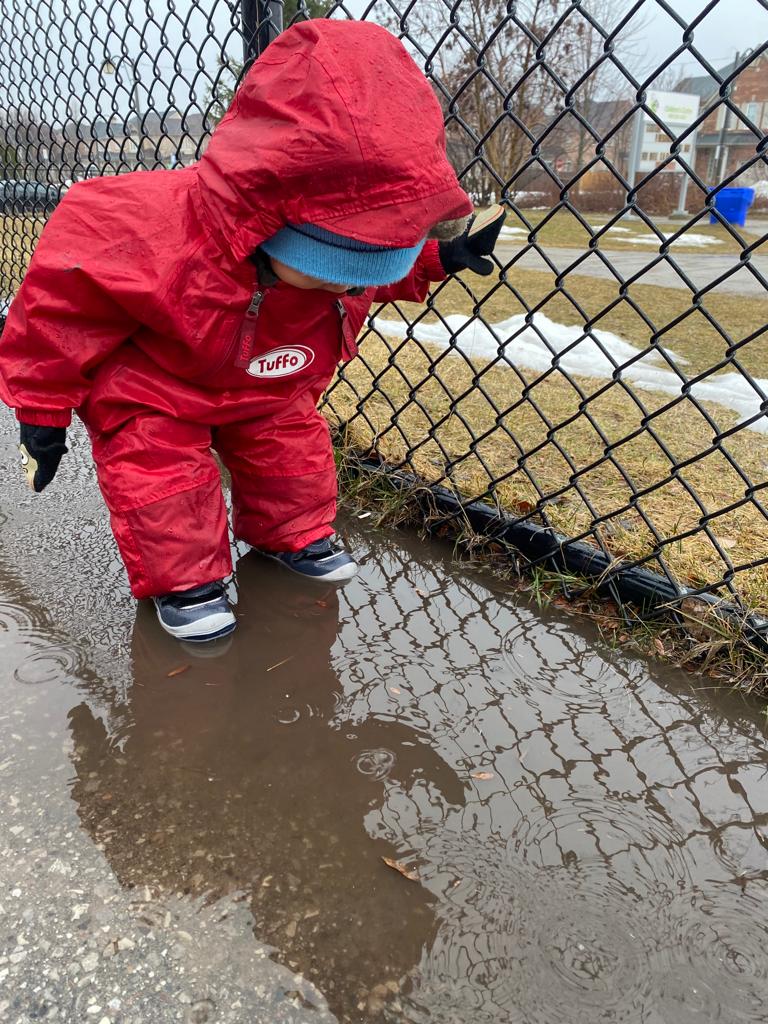 Toddler wearing splash suit, jumping in puddle