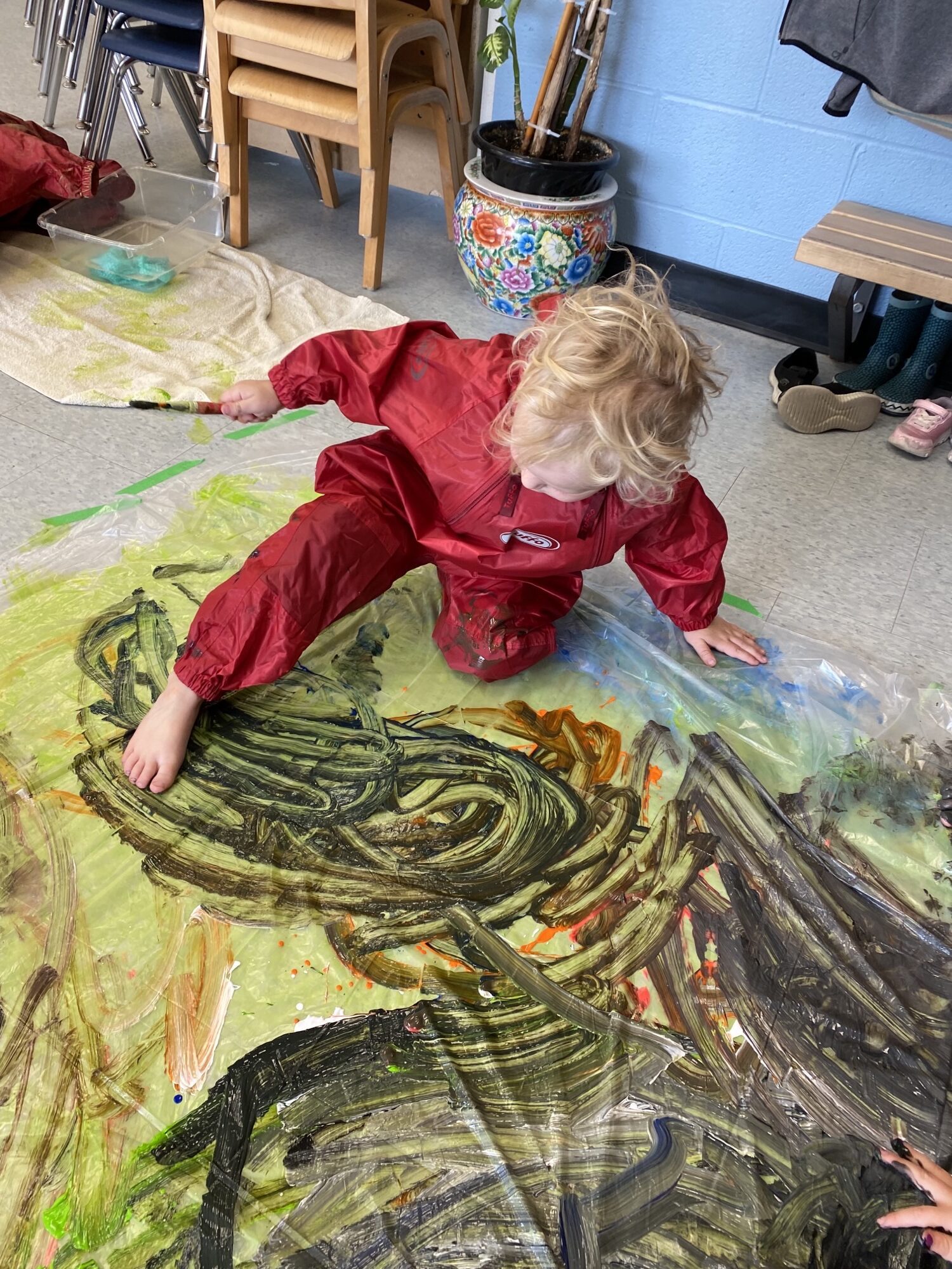 Preschool kid in a rainsuit with their foot in paint, doing an art activity
