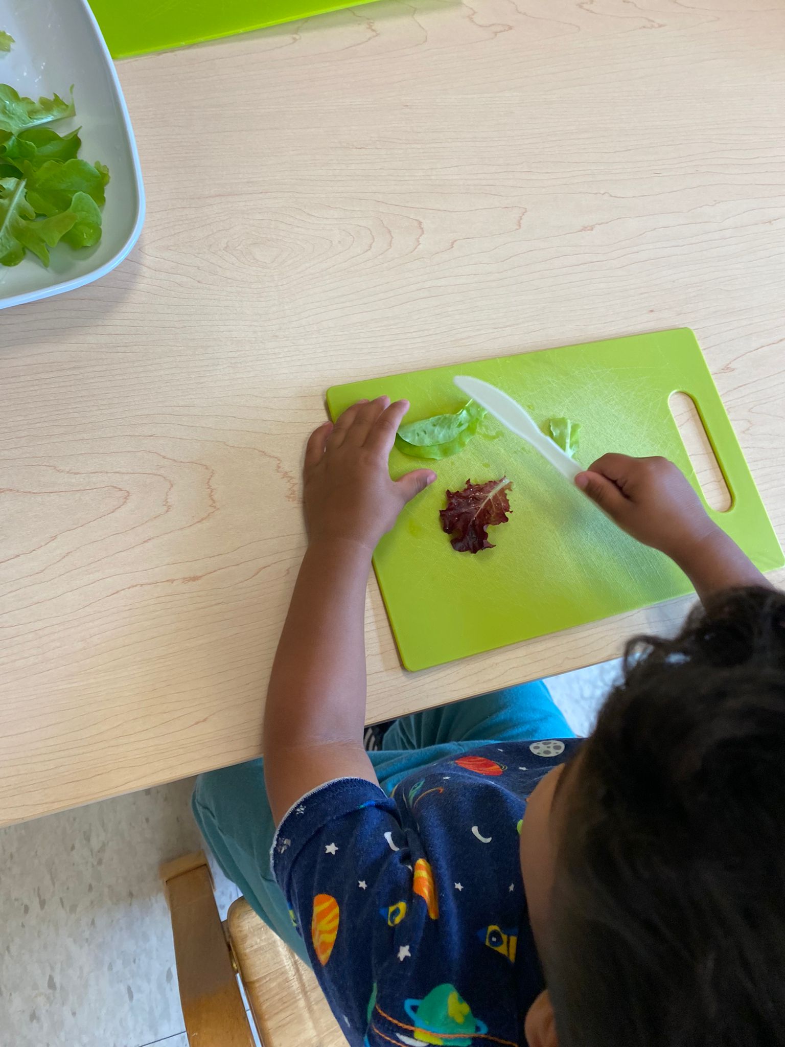 Child practicing cutting with plastic knife on cutting board