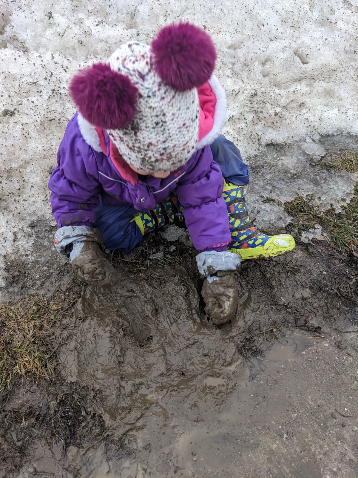 Child in snowsuit playing in snow and mud