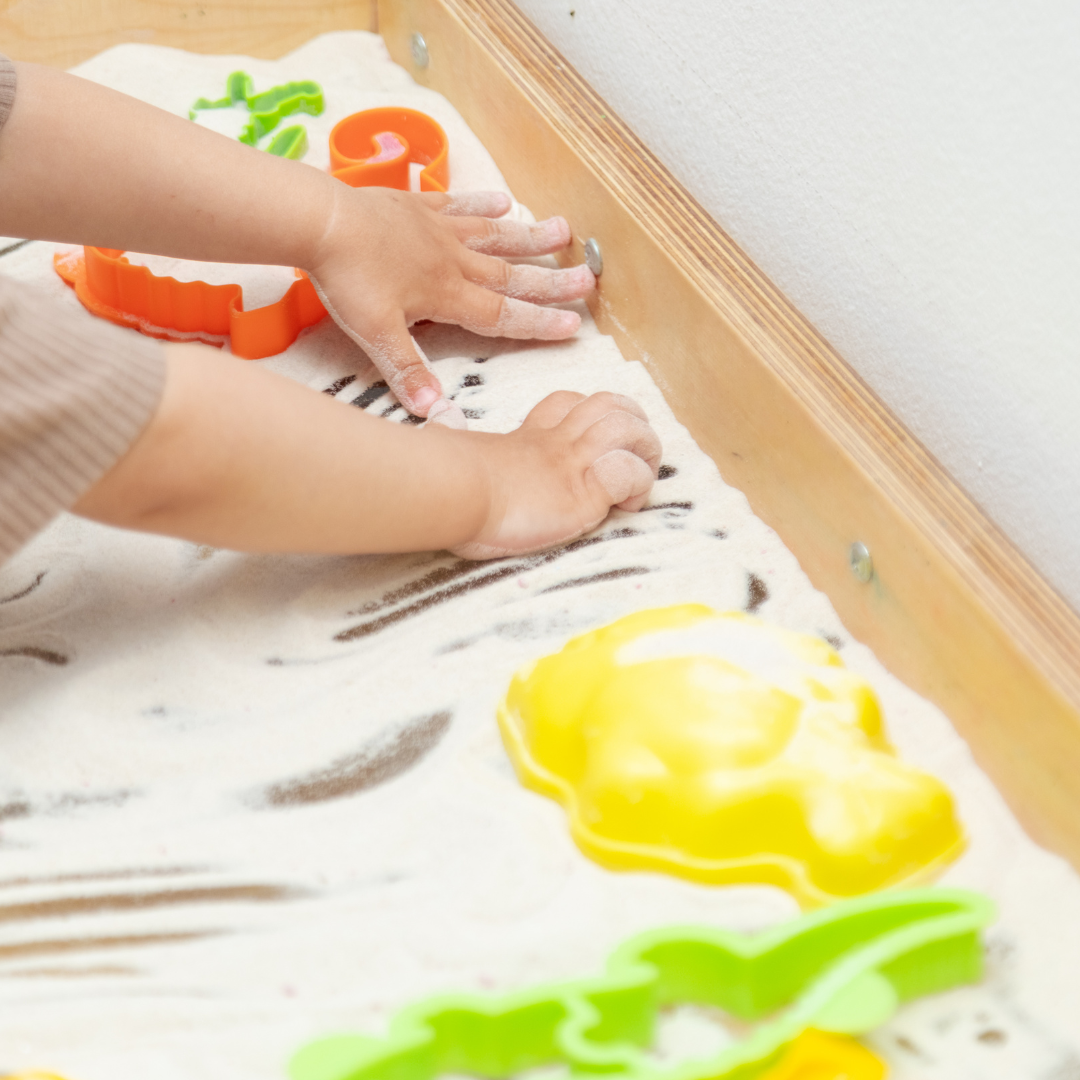 Child's hands playing in sensory sand table with toys