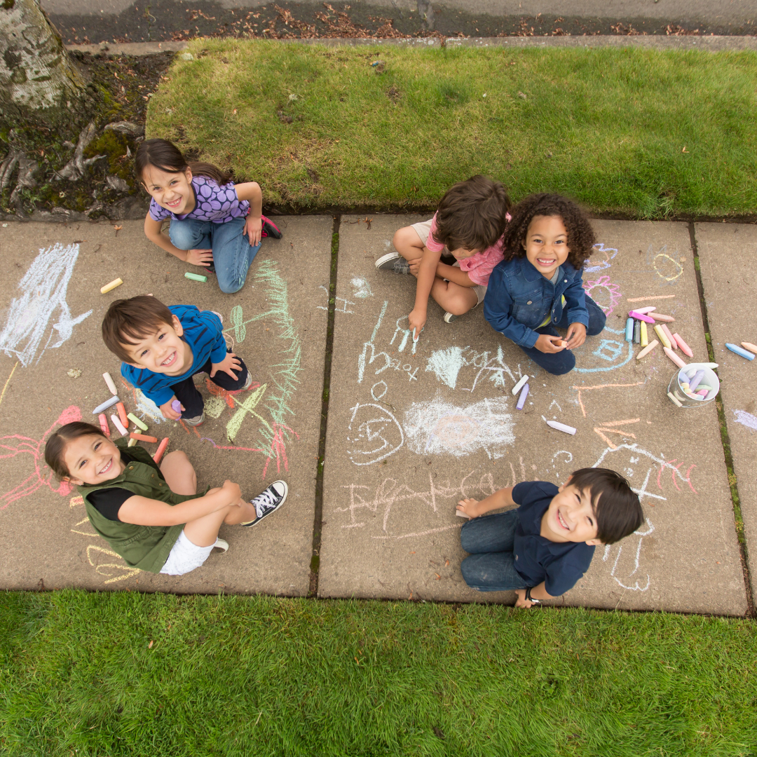 School age children sitting outside on sidewalk doing chalk drawings - Before and After School at Assikinack PS