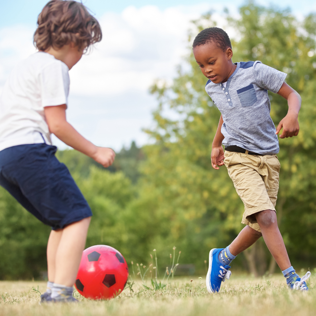 Two school age kids playing soccer outside