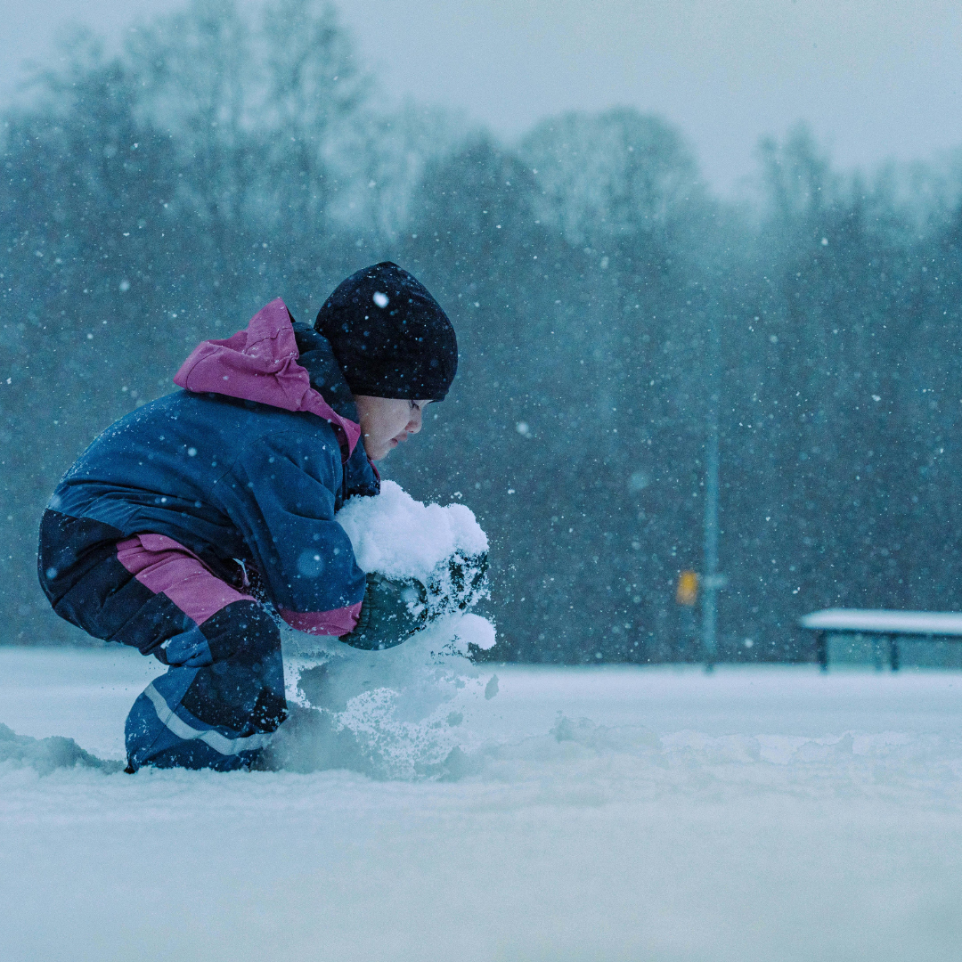Child building a large snowball outside