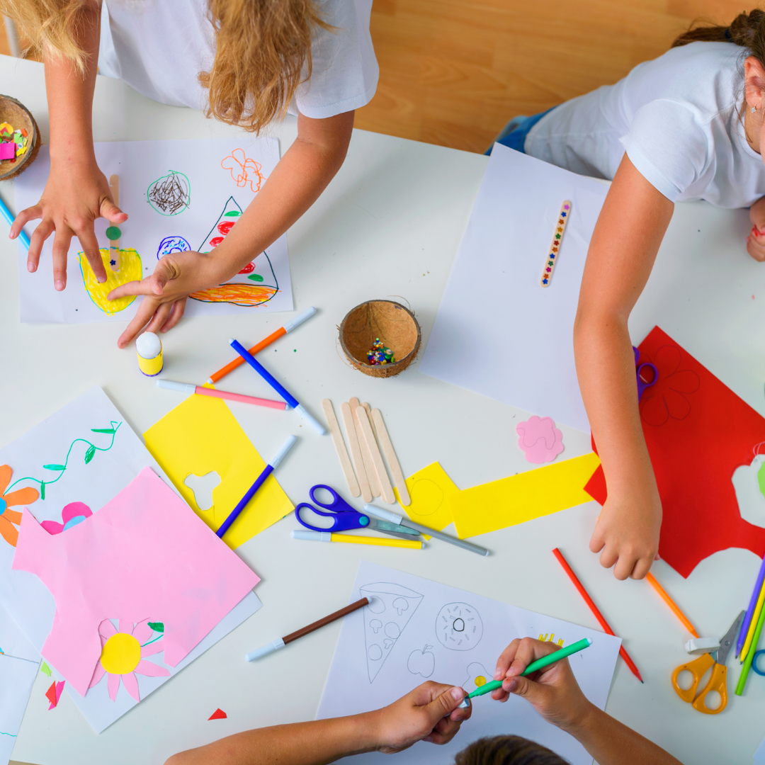 Children's arms doing arts and crafts at a table inside