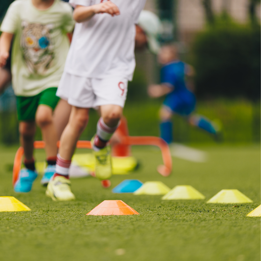 School age children doing physical outdoor activities: running through small pylon course on the grass