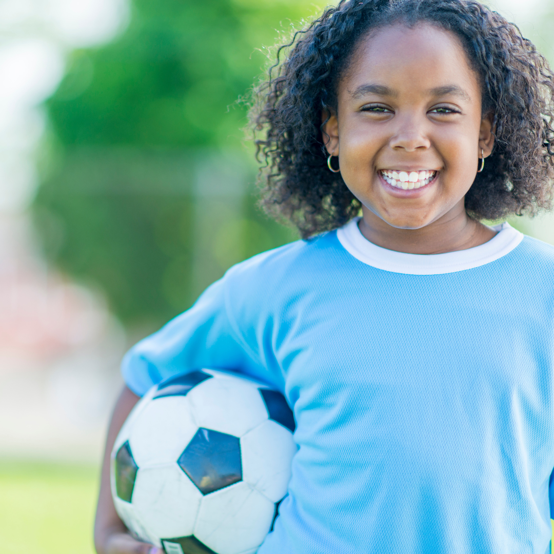 Smiling school age kid outside, holding a soccer ball