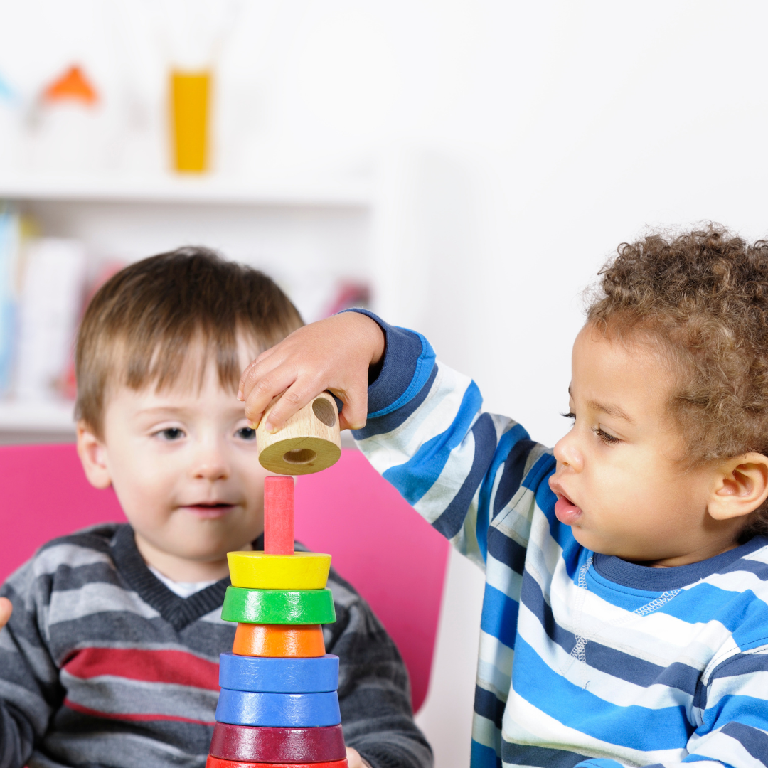 Two toddlers playing inside with wooden stacking toy