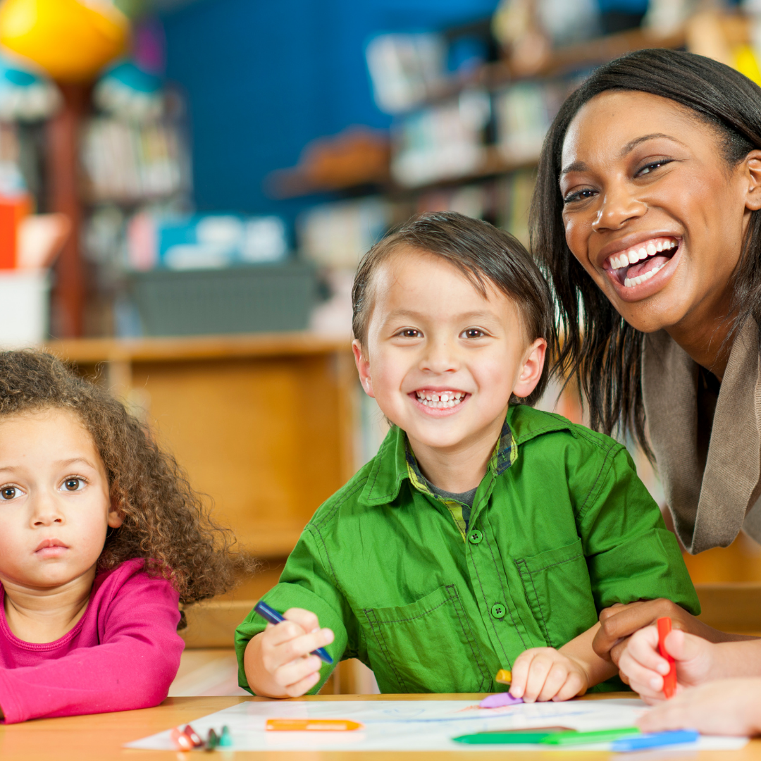 Smiling educator beside children doing table activities