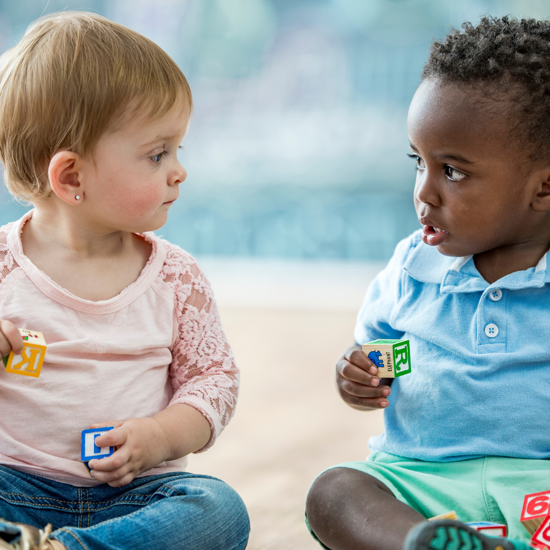 Two babies sitting, looking at each other