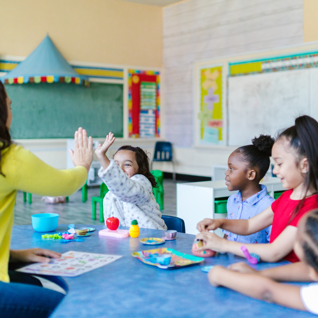 Children doing activities in a classroom. One child high fiving adult.