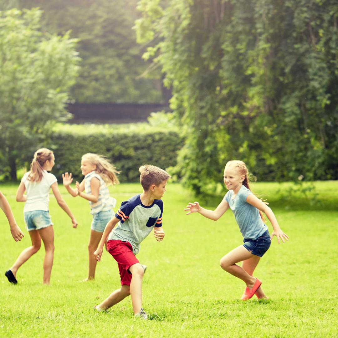School age children running and playing on the grass in a park