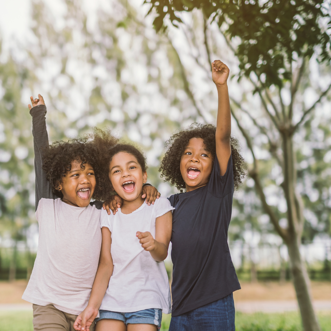 Smiling school age children outside with arms raised in the air