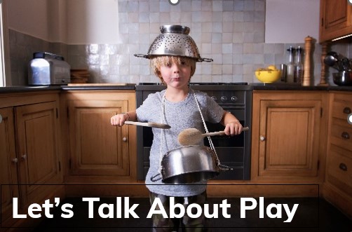 Child wearing a colander on their head in a kitchen while playing with pots and pans and spoons 