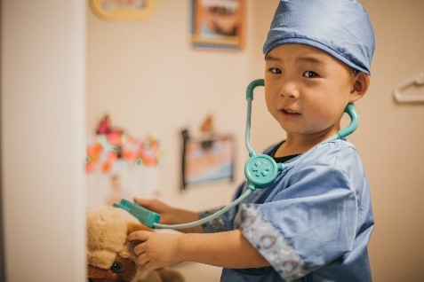 Child dressed up in a doctor's costume with stethoscope and taking care of a toy bear