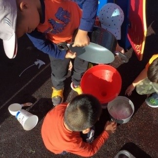 Several children doing water play with pots and containers outside in the school playground