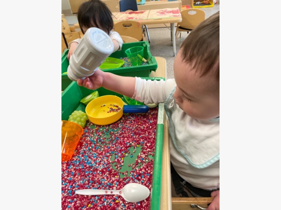 Two children playing in sensory bins filled with beads, containers, and spoons