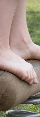 Child's bare feet, balancing on a log attached to a spring in a playground