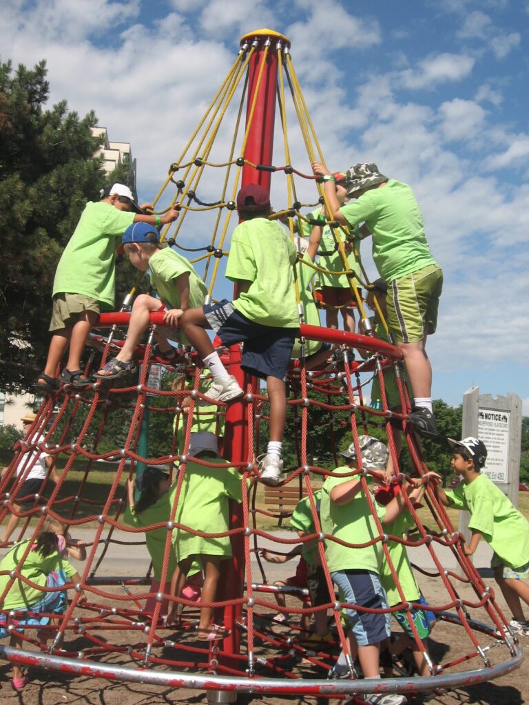 School age campers on a trip. Climbing a playground structure outside on a sunny day. 