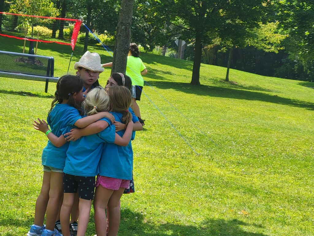 A group of 5 school age campers huddled together, playing in a park