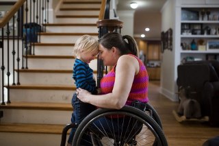 Child standing with adult in a wheelchair putting their heads together inside a house by a staircase 