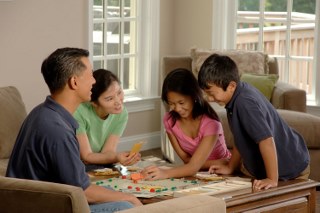Two adults and two children playing a boardgame in a house - all smiling
