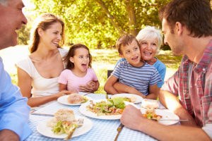 Two seniors, two adults, two children at a picnic table with food - everyone is smiling